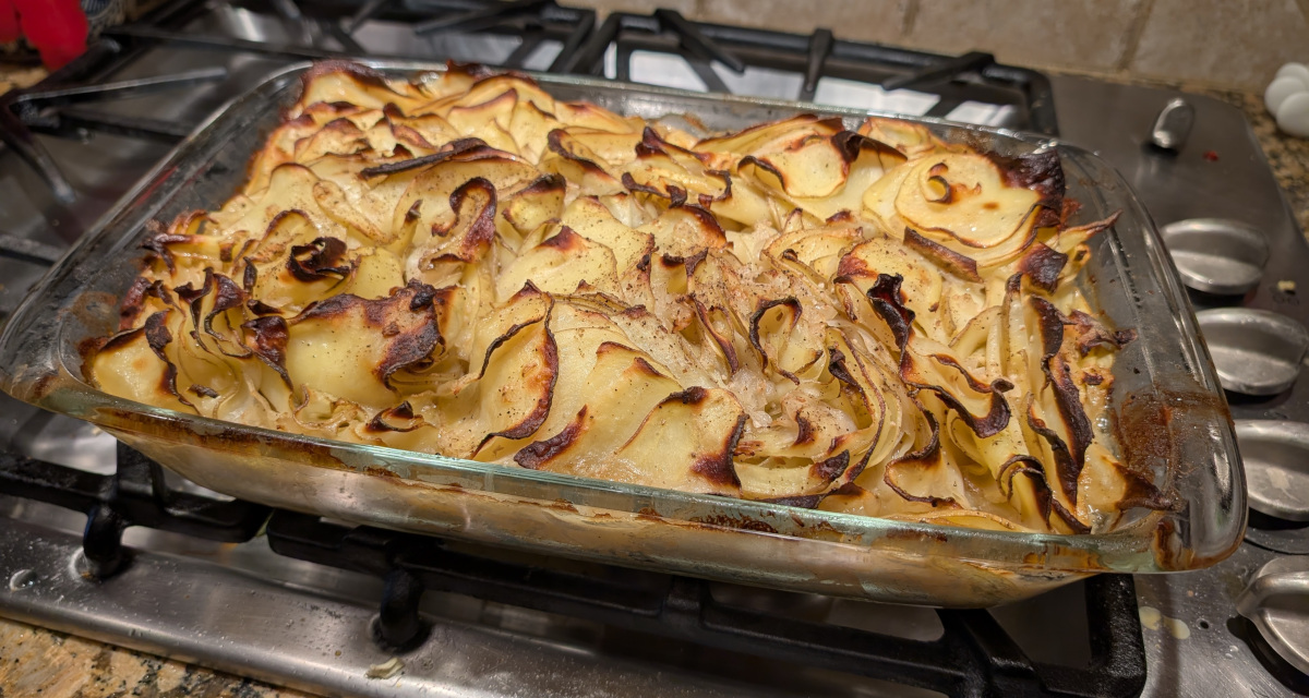 Casserole dish of baked potato slices resting on a stove, showing the randomly-layered top is crispy and browned while the edges are fully-baked