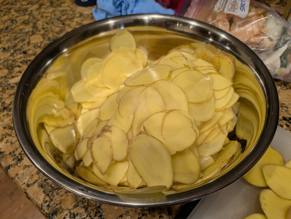 A large metal bowl full of potato slices