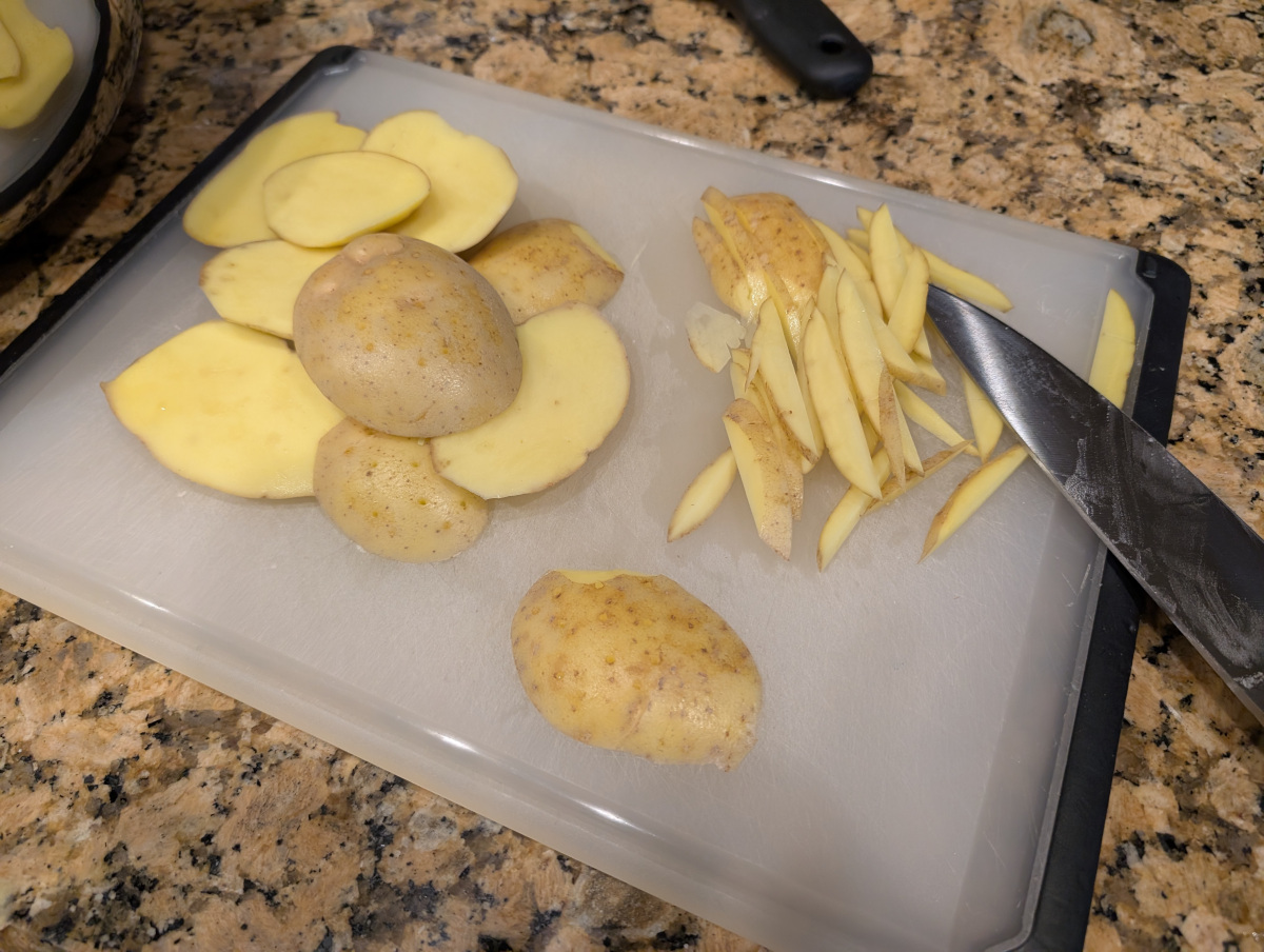 Ends of potatoes on a cutting board with some cut into strips with a chef's knife